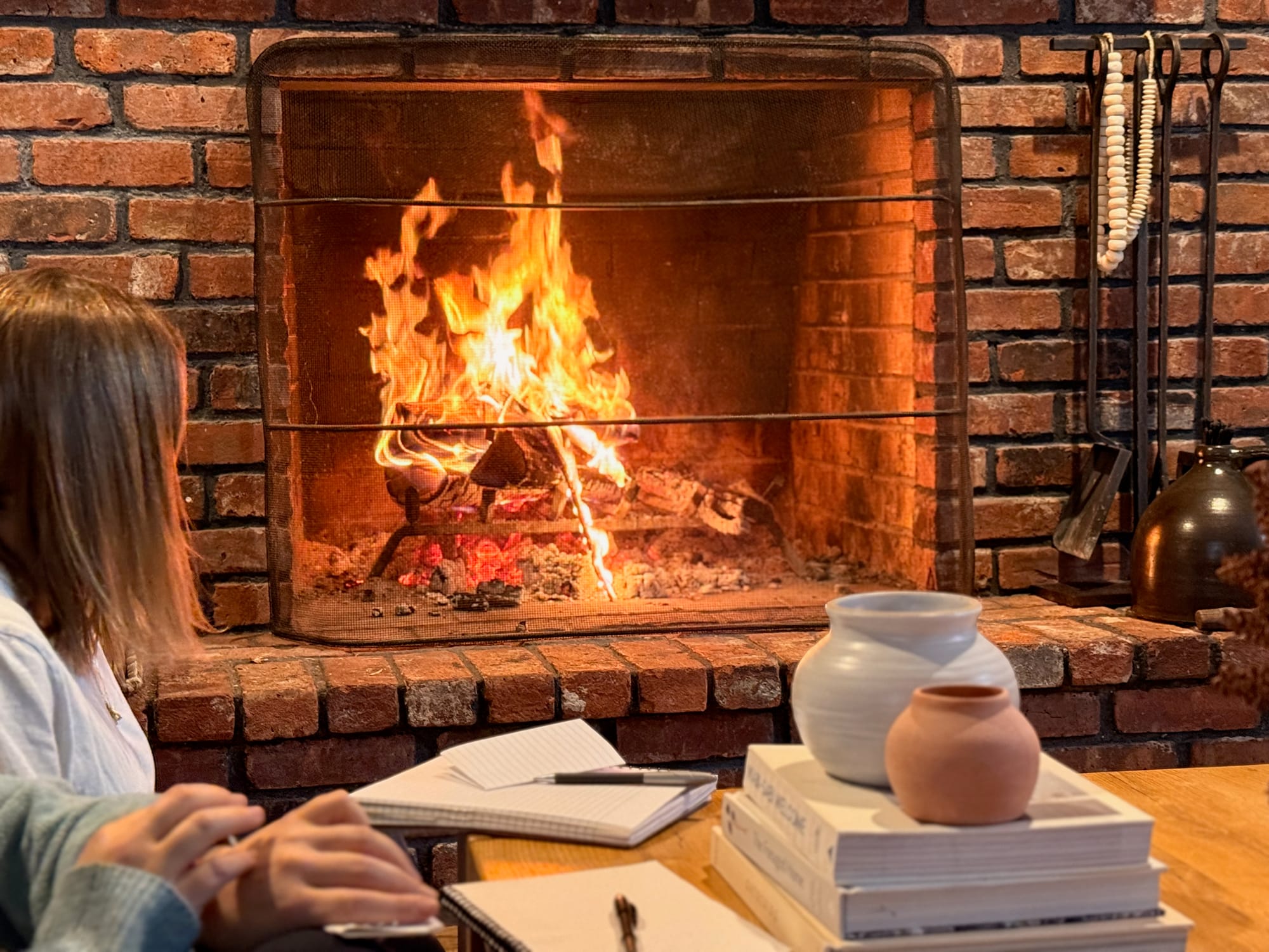 Women gaze into a fireplace with journals, pens, and ceramics in front of them