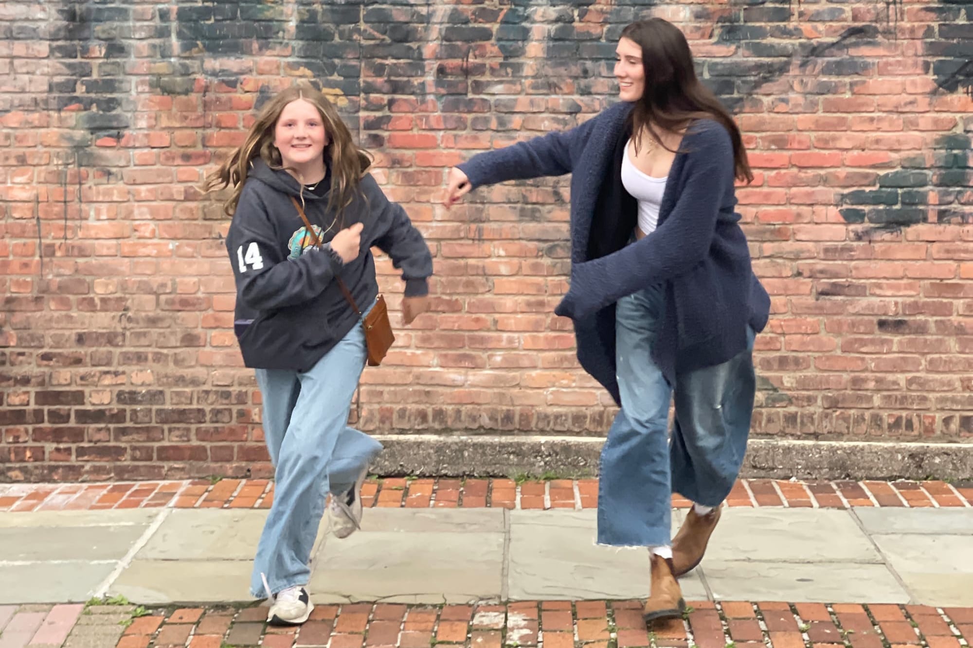 Two girls run with a red brick wall behind them