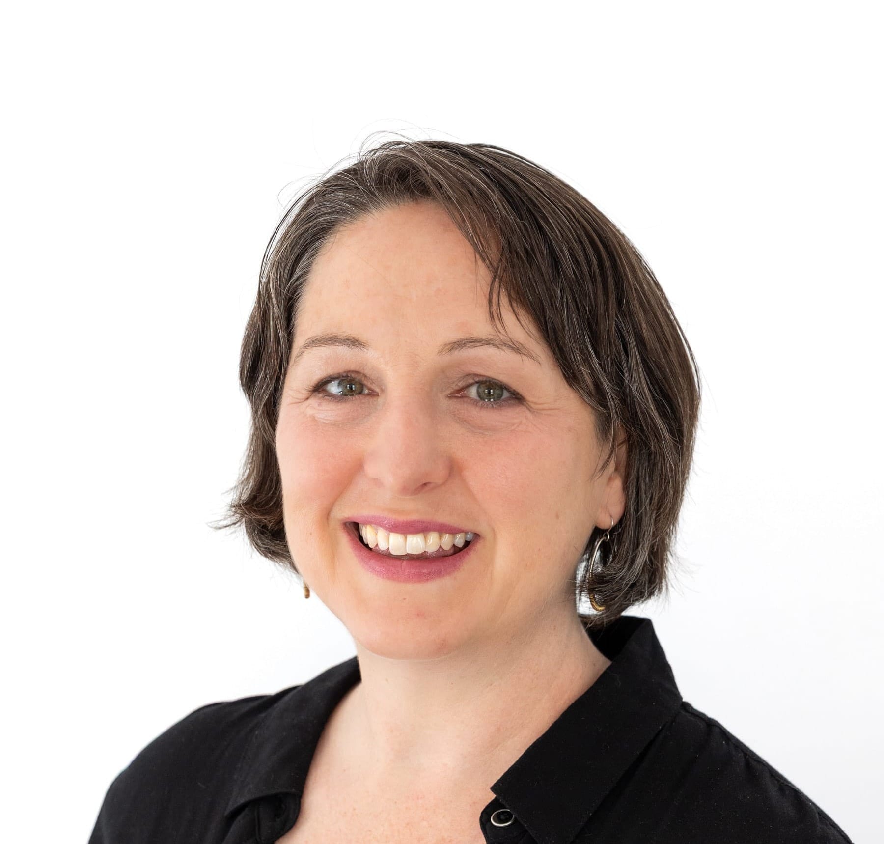 Woman with short graying hair and a black button-down shirt stands against a white background