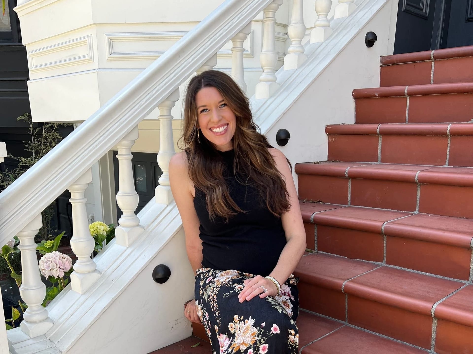 Radiant woman in a floral dress and white sneakers sits on terra cotta steps