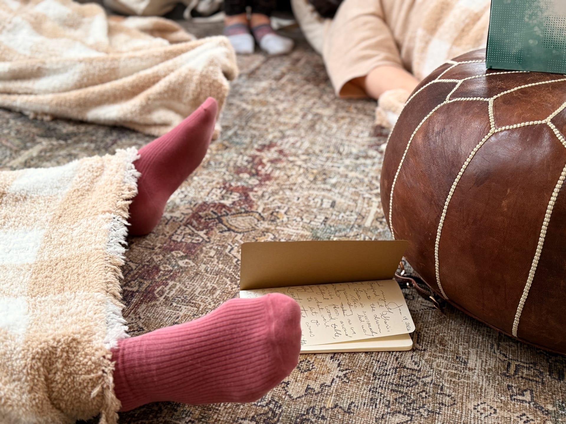 Blankets cover women resting, socks on feet sticking out by a journal on a patterned rug