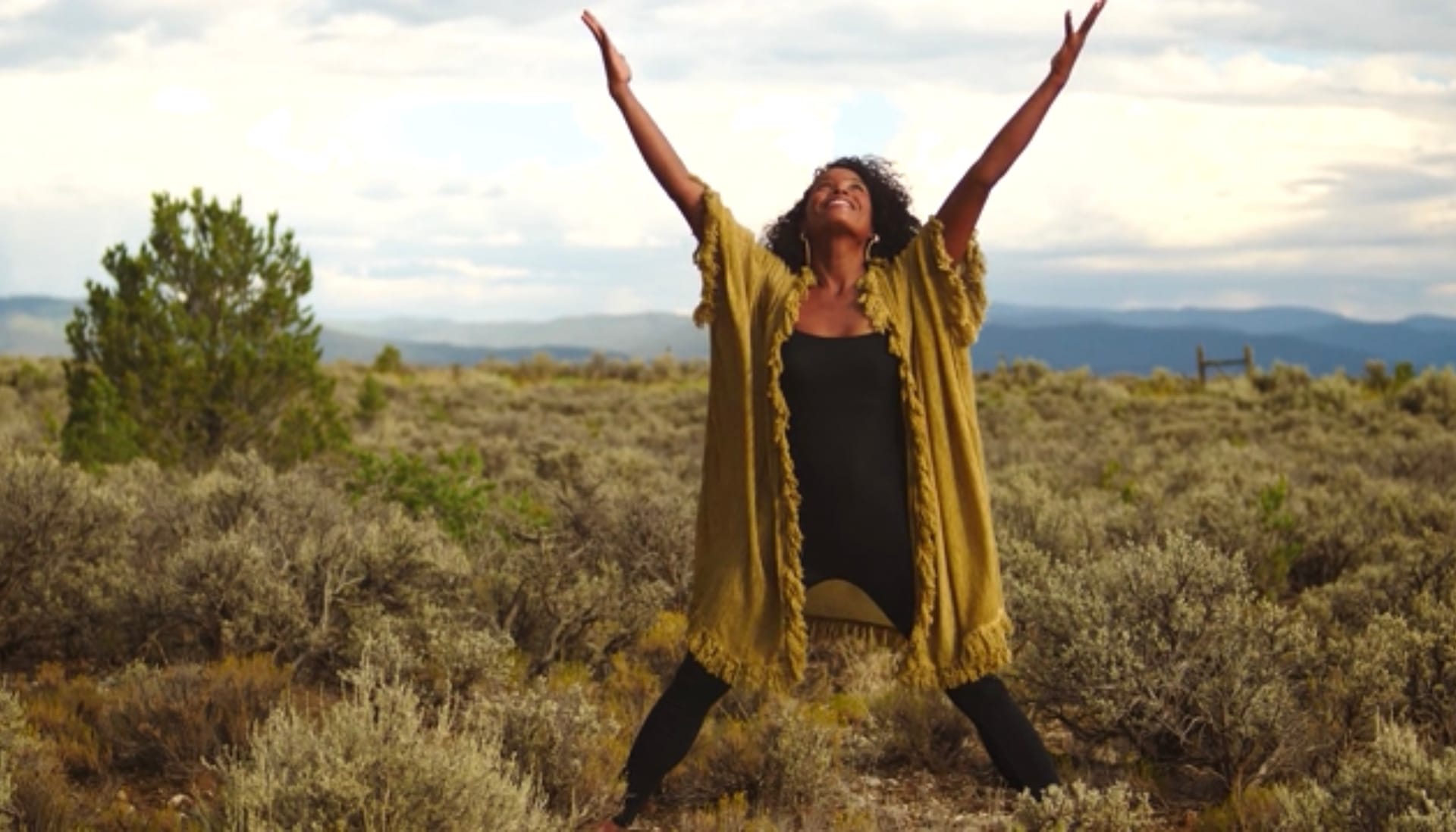 A black woman with with arms stretched overhead smiles towards the sky in a confident, open postu